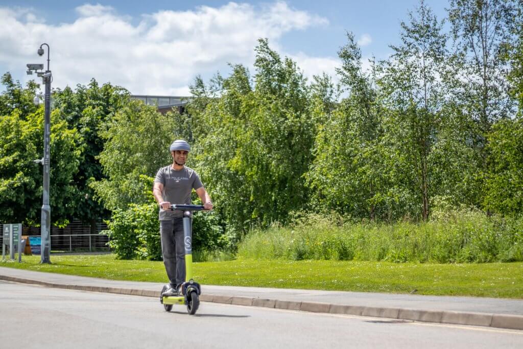 Person riding a trial E-scooter down a road wearing a helmet