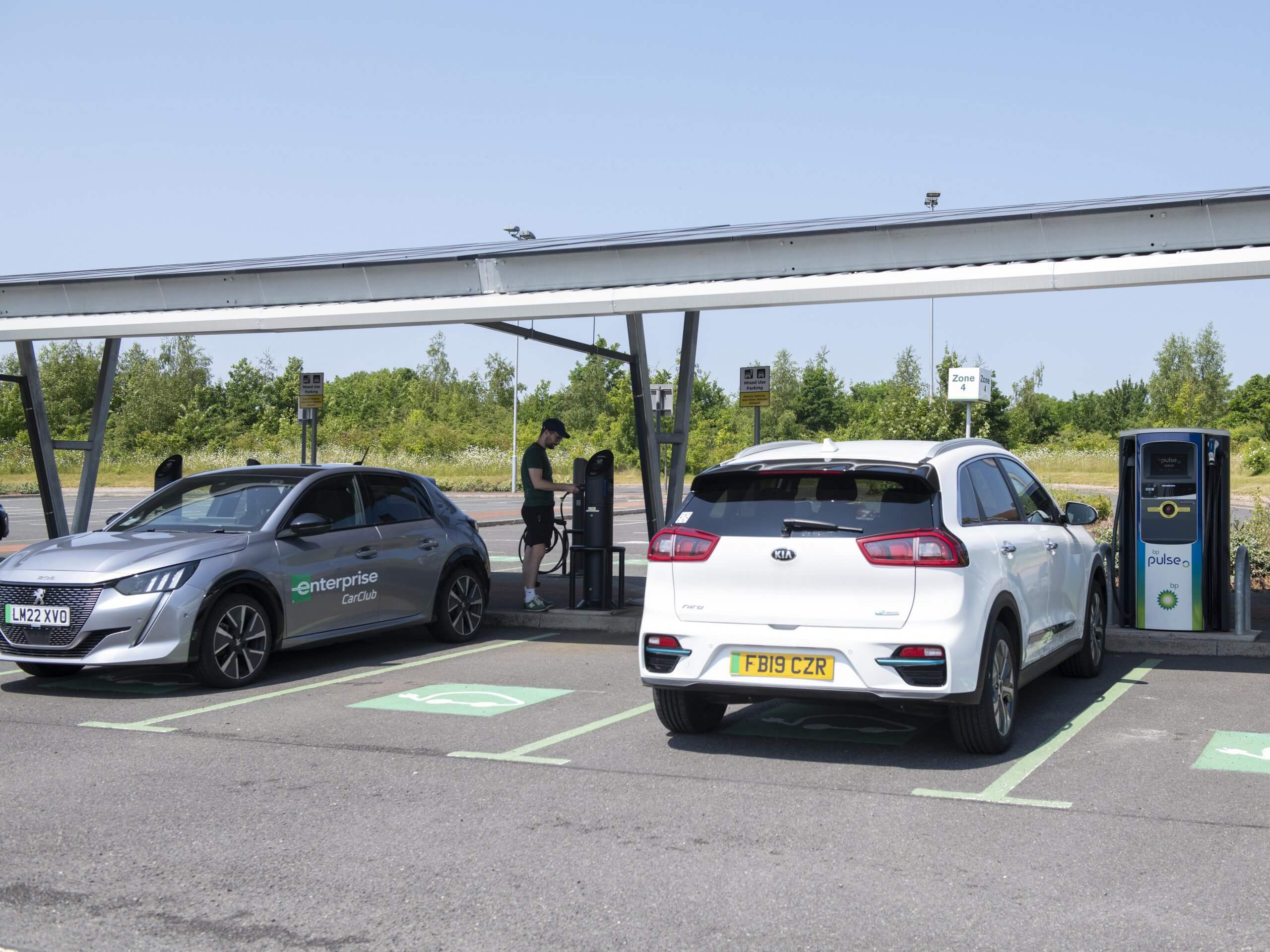 Two Electric Cars charging under a solar panel.