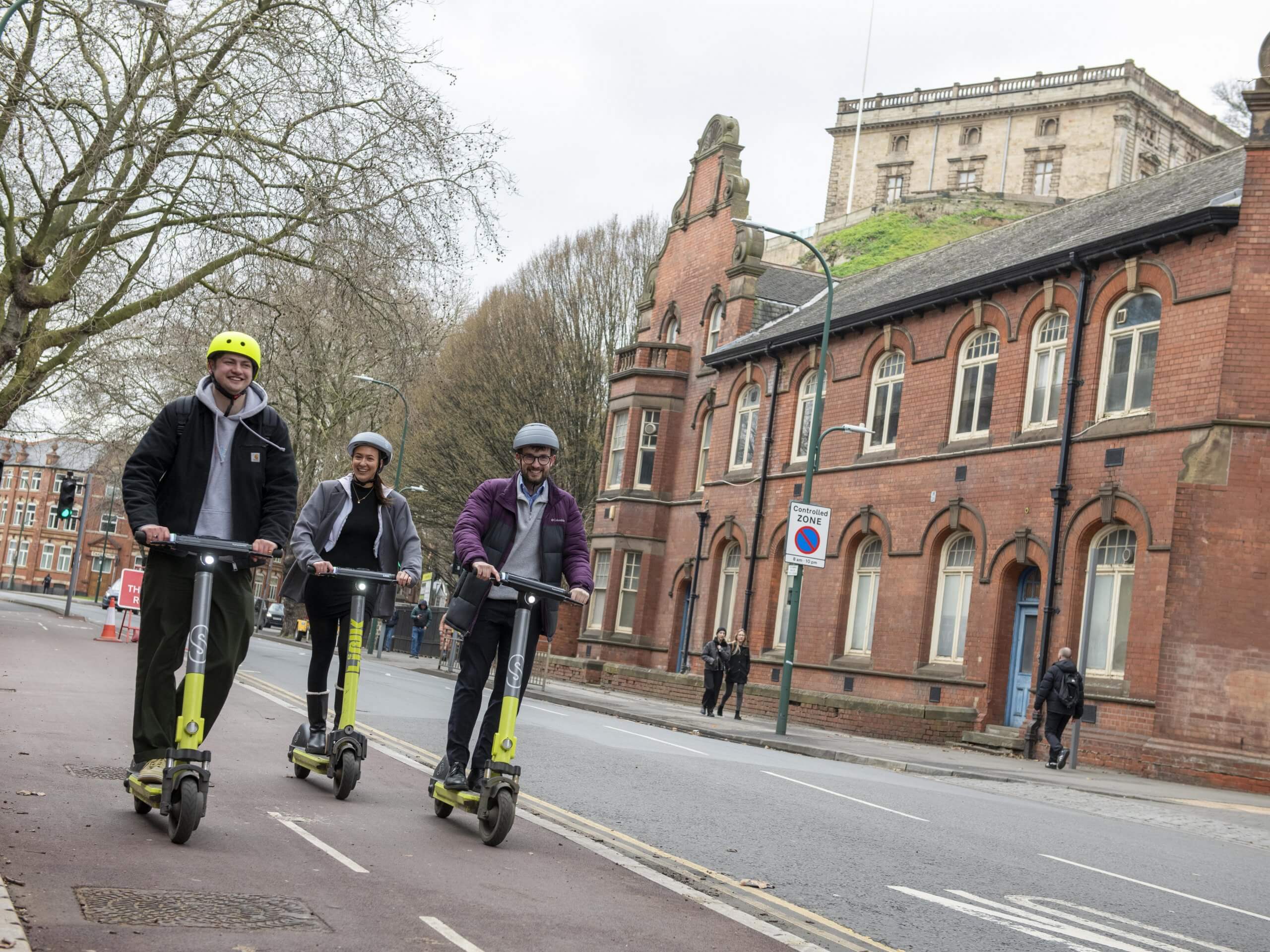 Three people on e-scooters with Nottingham Castle in the background