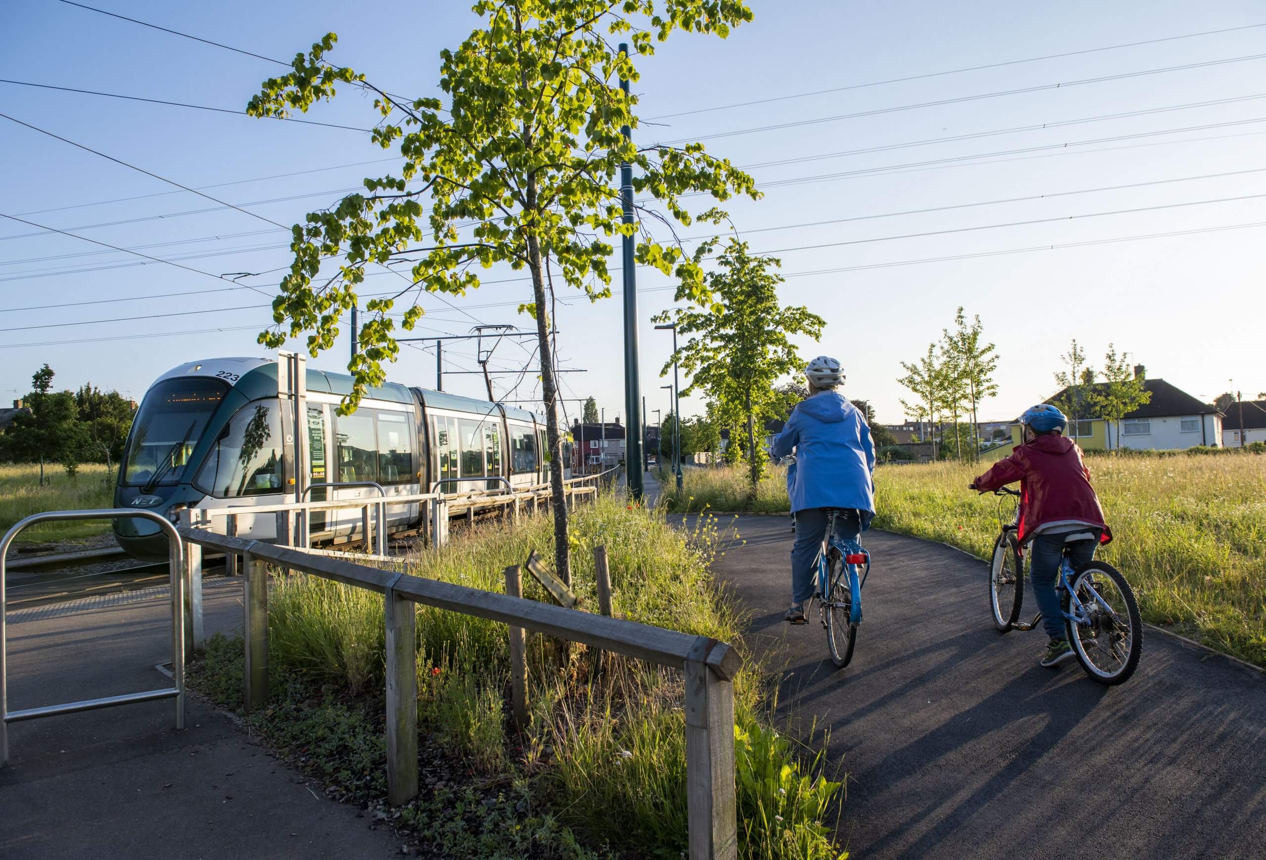 Adult and child cycling next to a tram