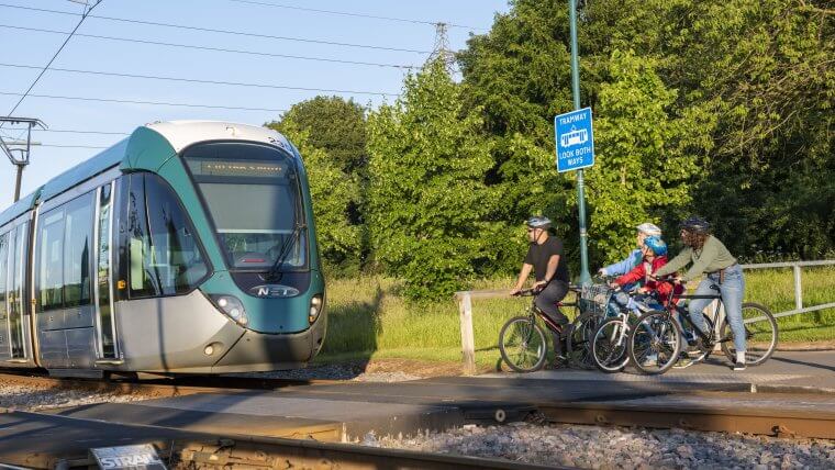 A family on bicycles wait for a tram to pass before crossing the tracks