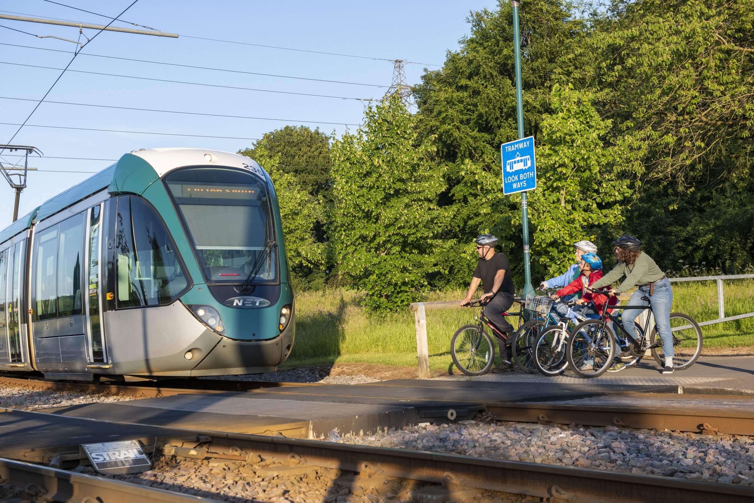 A family on bicycles wait for a tram to pass before crossing the tracks