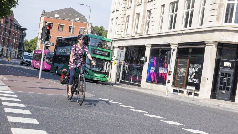 A lady cycles over a new cycle priority junction along Canal Street with a few buses waiting at the lights in the background on a sunny day